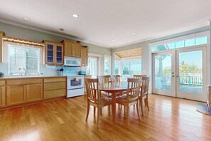 Cozinha com armários de madeira, mesa de jantar com cadeiras e uma grande porta de vidro deslizante que dá para um deck externo.