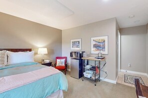 Een hotelkamer met een bed, bureau, stoel, koelkast en kunst aan de muur.
