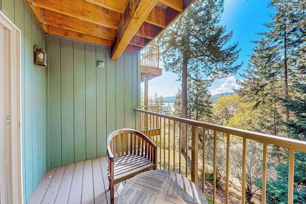 Eine Holzterrasse mit einer Bank, einem Geländer und Blick auf Wald und Berge.