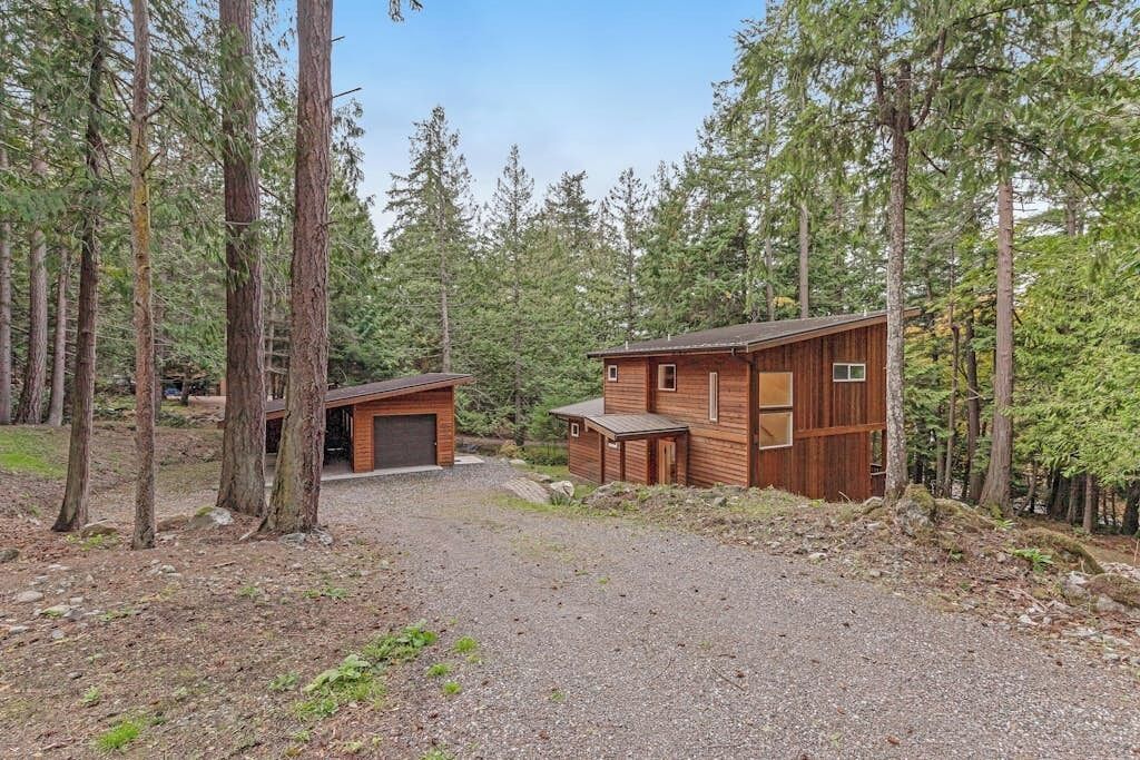 A cabin with a gravel driveway, surrounded by tall trees.