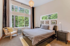 A bedroom with a large bed, a chair, a bedside table, and a window with a view of trees. - Pet Friendly Forest Retreat with Modern Amenities and Fast WiFi in Eastsound (Eastsound)