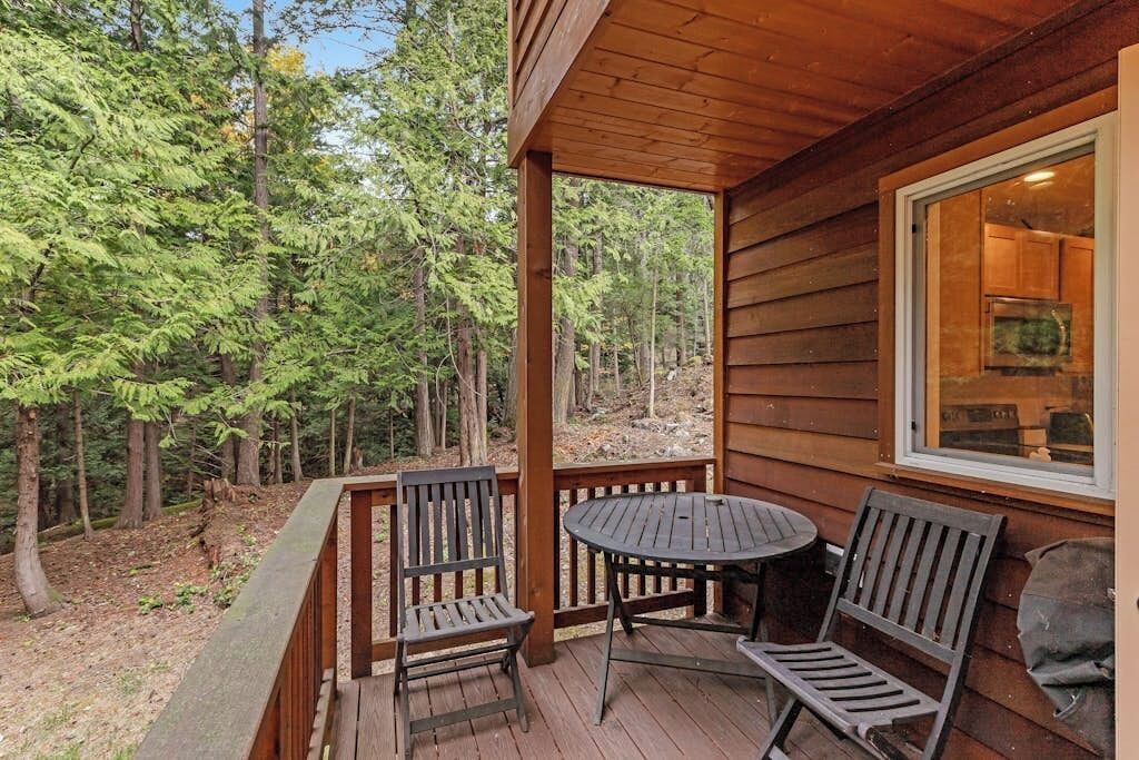 A wooden deck with two chairs and a table, overlooking a forested area.