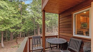 Una terraza de madera con dos sillas y una mesa, con vista a un área boscosa.