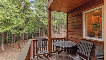 A wooden deck with two chairs and a table, overlooking a forested area.