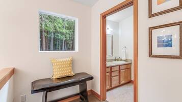 Un pasillo con un banco, una ventana con vistas a árboles y un baño visible a través de una puerta abierta.