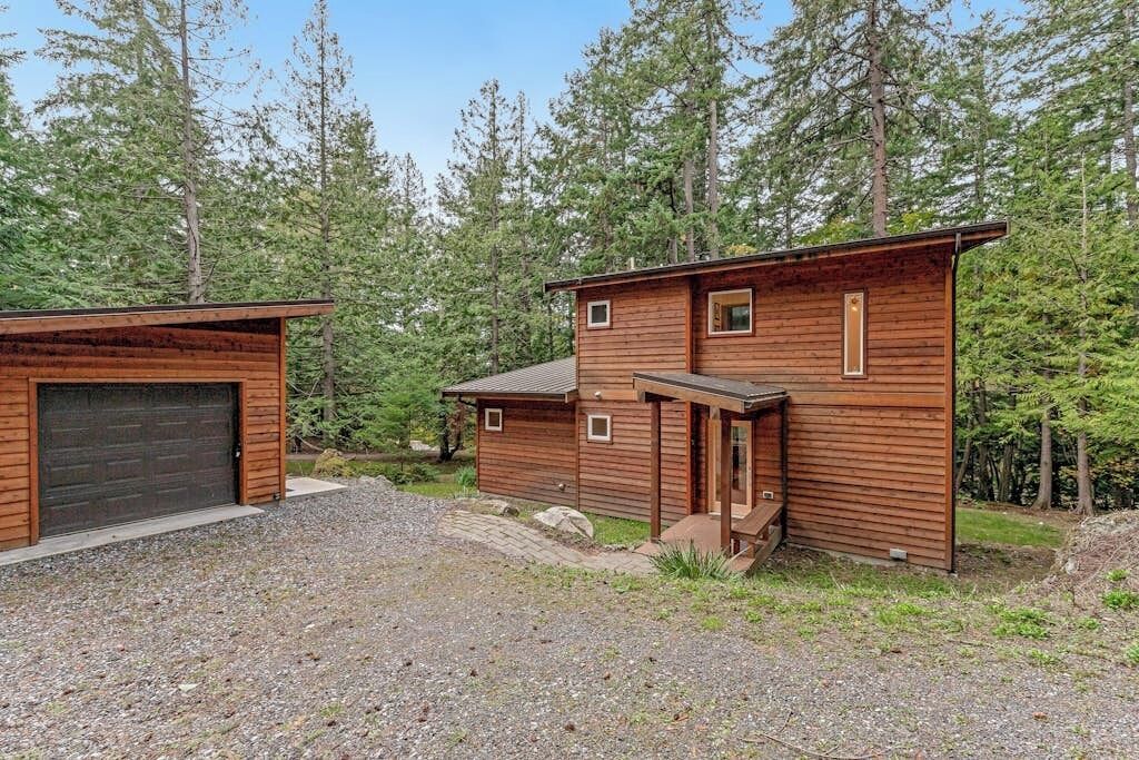 A two-story wooden cabin with a garage, surrounded by a forested area.