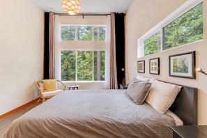 Un dormitorio con una cama grande, una silla, una mesita y varias ventanas.