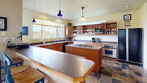 A modern kitchen with a central island, wooden cabinets, and a black refrigerator. - Spacious, Modern House with Stunning Bay Views - Lopez Village and Marina (Lopez Island)
