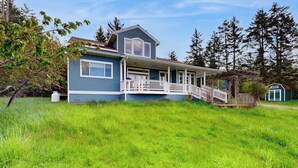A two-story house with a porch and a small shed in the background. - Spacious, Modern House with Stunning Bay Views - Lopez Village and Marina (Lopez Island)