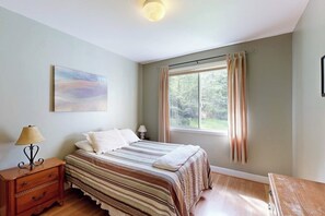 A bedroom with a bed, nightstands, a window with curtains, and a painting on the wall.