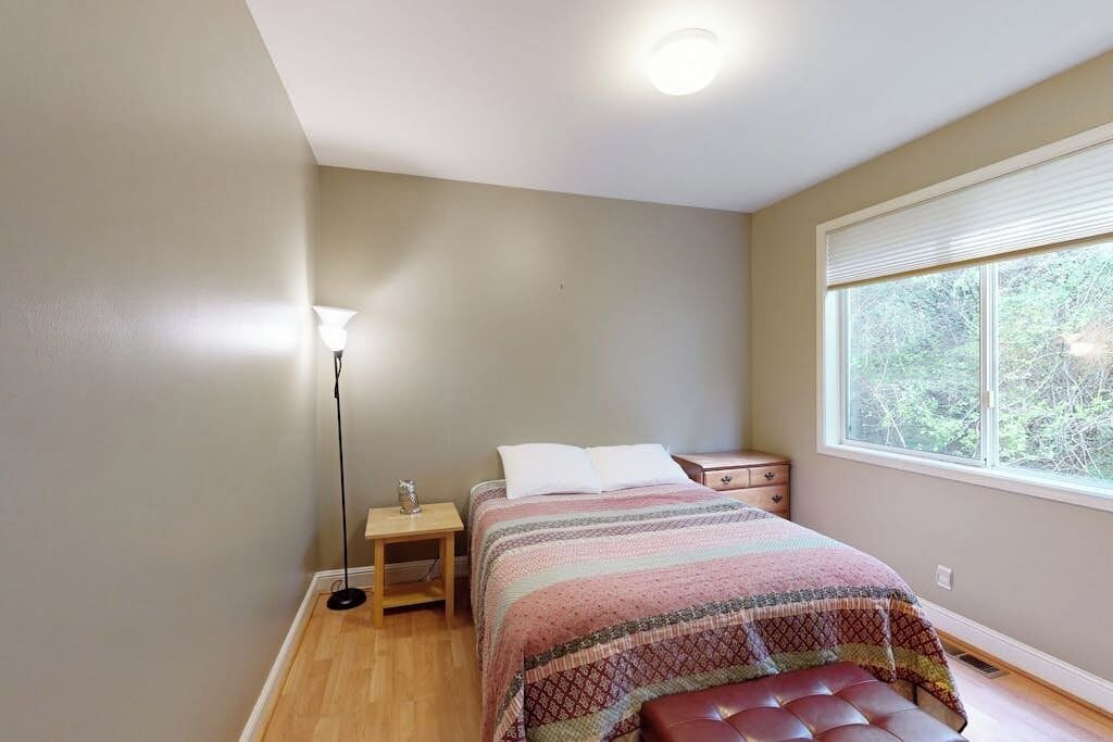 Een slaapkamer met een bed, nachtkastje, lamp en raam.