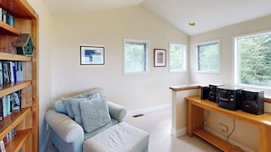 A room with a light blue sofa, wooden bookshelves, a wooden desk with speakers, and framed pictures on the wall. - Spacious, Modern House with Stunning Bay Views - Lopez Village and Marina (Lopez Island)