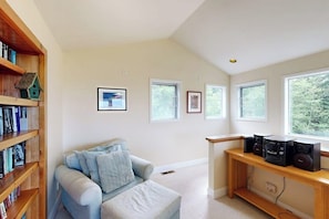 Een kamer met een lichtblauwe bank, houten boekenkasten, een houten bureau met speakers en ingelijste foto’s aan de muur.