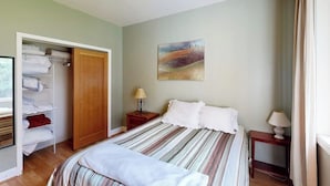 A bedroom with a bed, a wardrobe, a nightstand, a lamp, and a painting on the wall. - Spacious, Modern House with Stunning Bay Views - Lopez Village and Marina (Lopez Island)