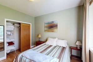 Een slaapkamer met een bed, een kledingkast, een nachtkastje, een lamp en een schilderij aan de muur.