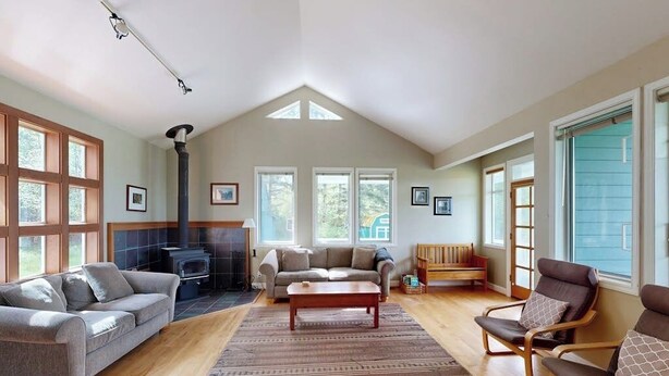 A spacious living room with a fireplace, a sofa, a coffee table, and a large window. - Spacious, Modern House with Stunning Bay Views - Lopez Village and Marina (Lopez Island)