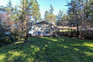 A rustic cabin with a sloped roof, surrounded by a wooden fence and dense trees.