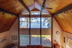 A room with a sloped ceiling, large windows, and a view of a dock and water.