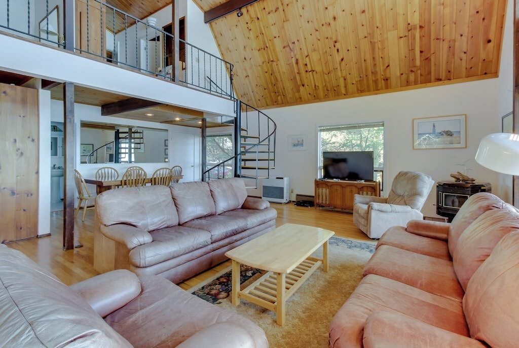 A spacious living area with a high ceiling, a staircase, and a television.