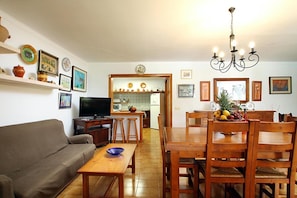 Uma sala de estar com sofá, mesa de centro, televisão e área de jantar com mesa e cadeiras.