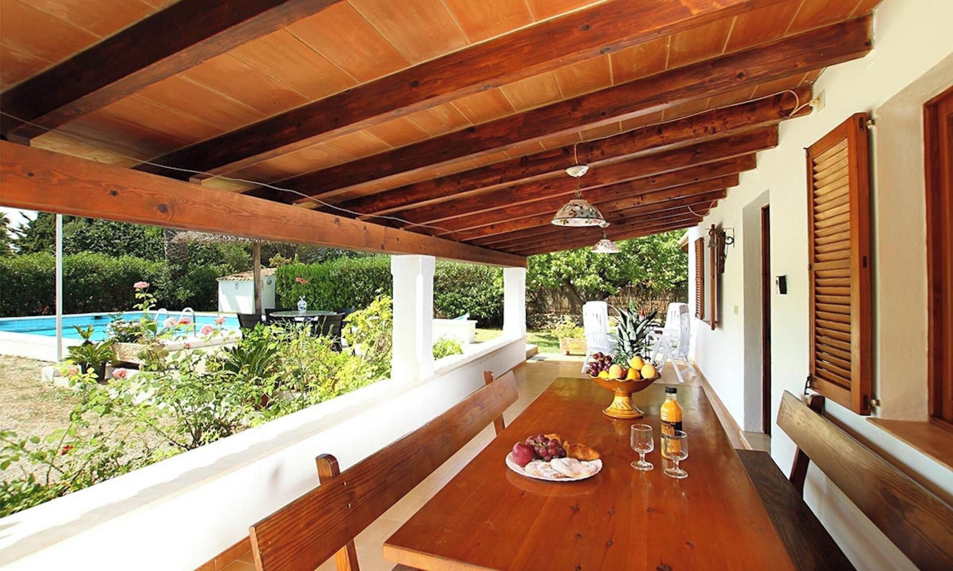 Une terrasse extérieure en bois, avec une table dressée pour les repas, donnant sur une piscine et sur un espace verdoyant.
