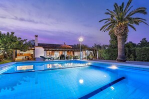 Ein Swimmingpool mit klarer, blauer Wasseroberfläche, umgeben von einem Haus mit einem Ziegeldach und einer Strohbedeckung.