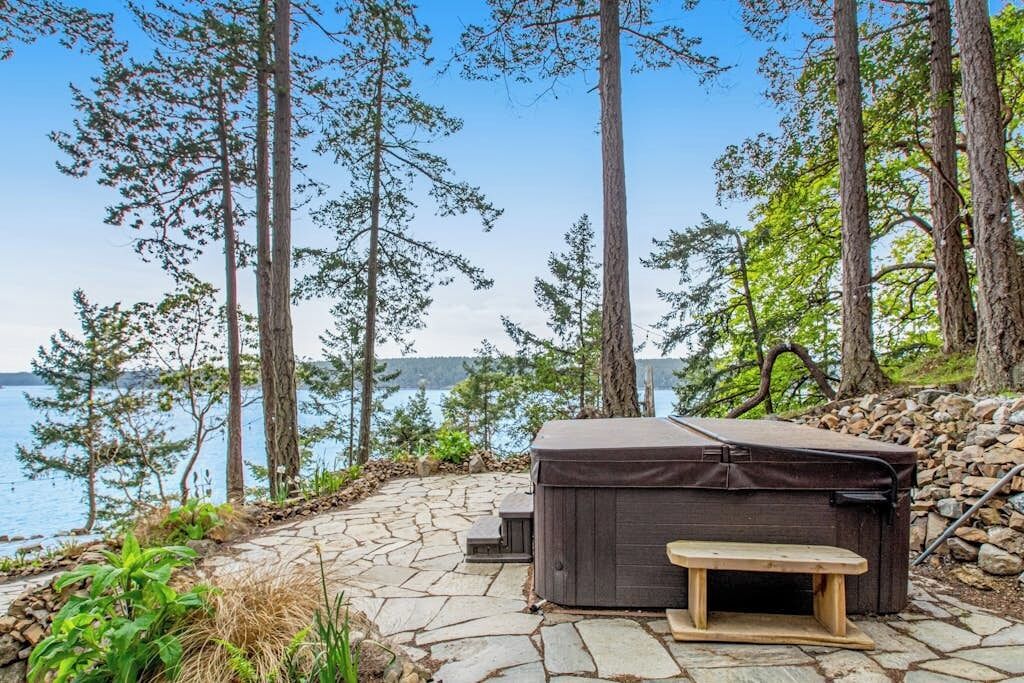 Een hottub en een bankje op een terras van natuursteen met uitzicht op een meer.