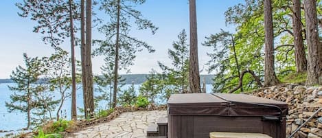 Een hottub en een bankje op een terras van natuursteen met uitzicht op een meer.
