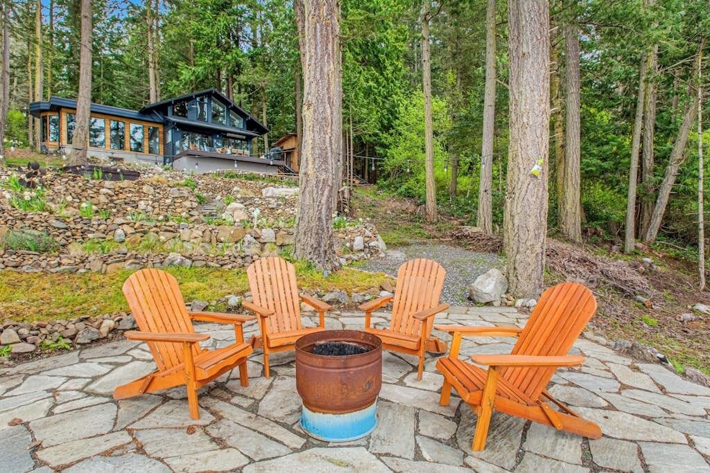 A stone patio with four wooden Adirondack chairs and a central fire pit.