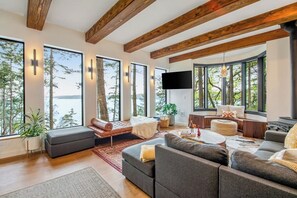 A modern living room with large windows, a flat-screen TV, and a fireplace. - Stylish Waterfront Oasis with Hot Tub, Fiber Optic Internet, and Entertainer's Deck (Lopez Island)