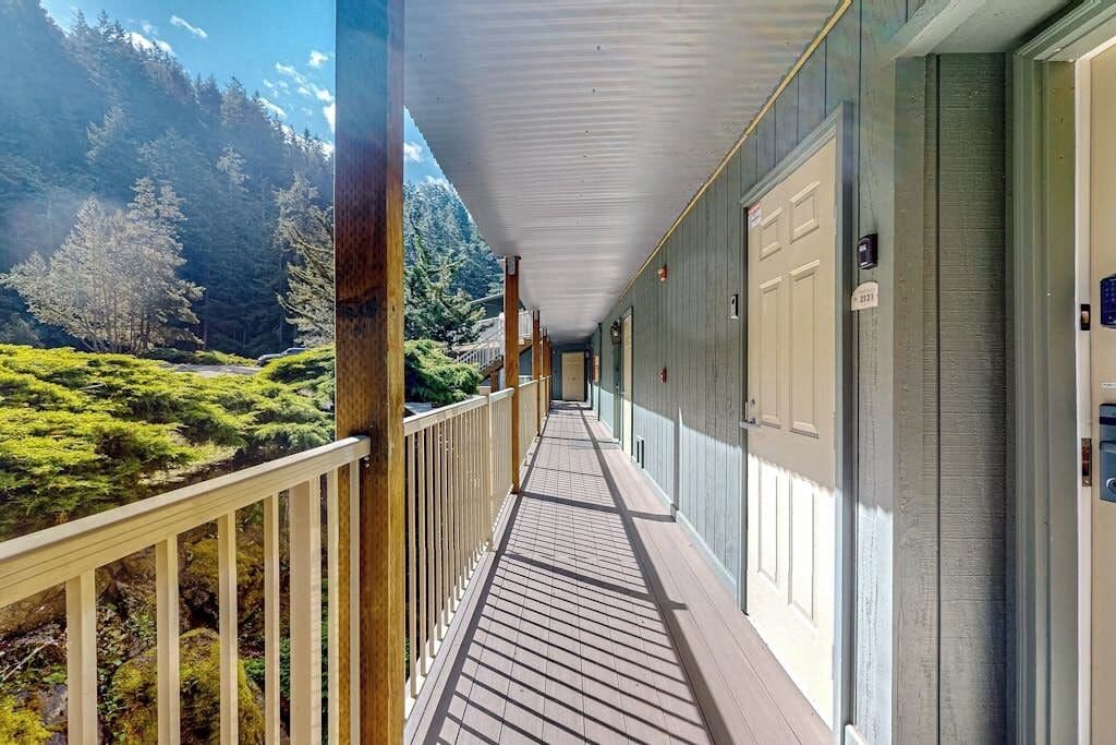 Un pasillo con cubierta de madera que conduce a un edificio con una puerta, rodeado por un paisaje boscoso.