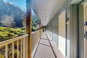 A corridor with a wooden deck leading to a building with a door, surrounded by a forested landscape.
