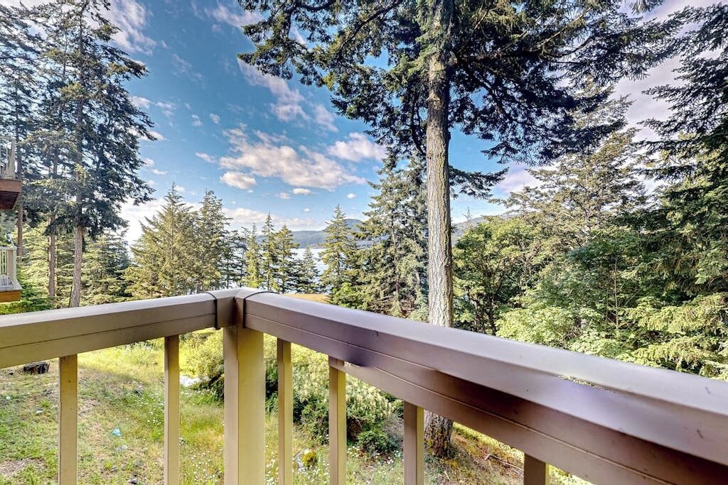 Une balustrade en bois sur une terrasse, offrant une vue sur un paysage boisé et des montagnes au loin.