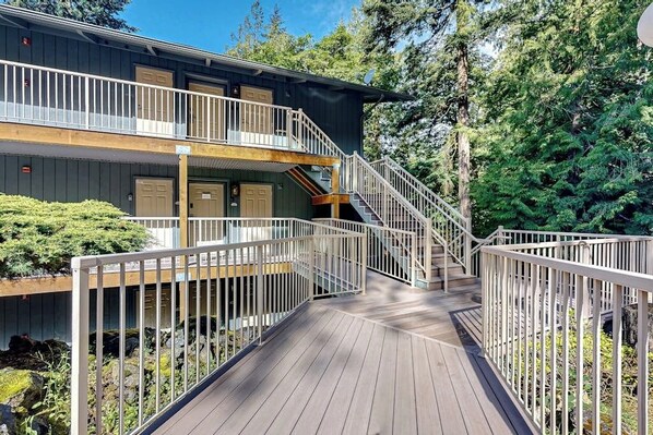 Un edificio de dos pisos con una terraza de madera y una escalera que conduce al nivel superior.