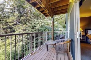 A wooden deck with a railing, a table, and two chairs, overlooking a forested area.
