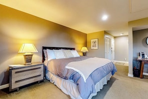 A bedroom with a bed, bedside lamps, a nightstand, and a door leading to another room.