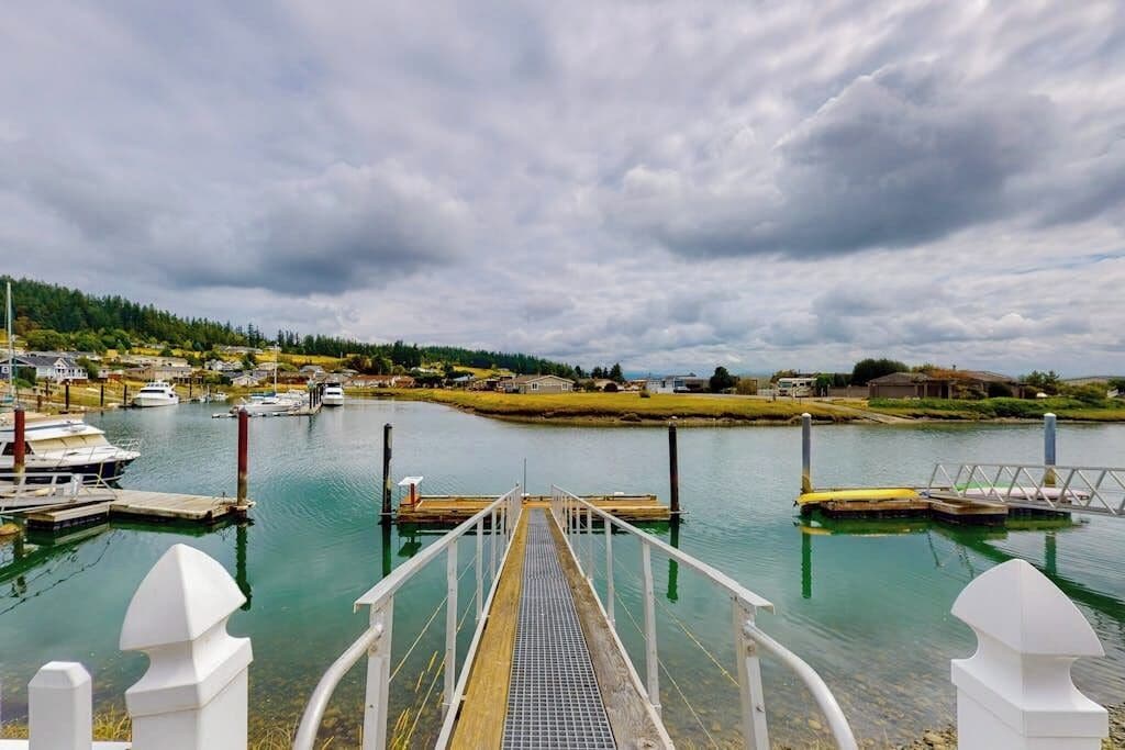 Ein Yachthafen mit vertäuten Booten, eine Holzstege zum Wasser und eine kleine Insel mit Gebäuden im Hintergrund.