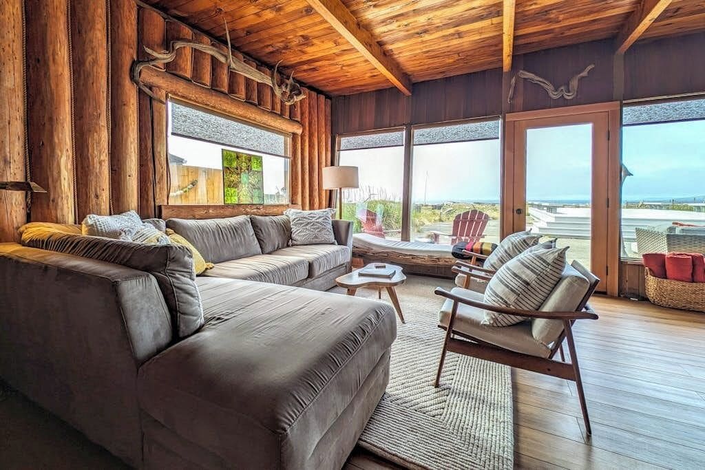 A log cabin interior with a sofa, armchair, and a view of the outdoors.