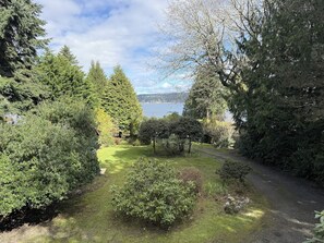 A landscaped garden with a variety of trees and shrubs, a clear sky, and a body of water in the background. - Cozy Island Retreat near Beaches, Trails, and Langley! (Langley)