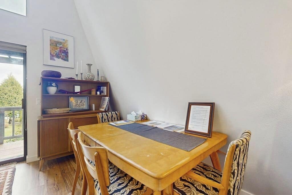 A dining area with a wooden table and chairs, a framed menu, and a shelf with various items.