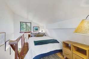Un dormitorio con una cama, una mesita de noche de madera, una lámpara y una ventana con persianas.