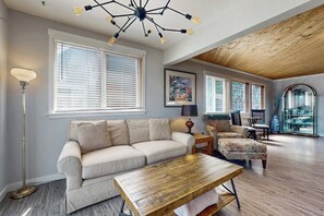 Un salon avec un canapé, une table basse et une lampe. Il y a un luminaire au plafond et une fenêtre avec des stores.
