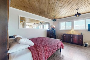 A bedroom with a wooden ceiling, a bed with white and red bedding, a dresser, and a mirror. - Relaxing Waterfront Studio Cottage with Private Beach Access (Clinton)