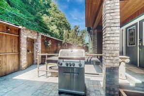 A patio with a stainless steel grill, a brick wall, and a wooden fence. - Relaxing Waterfront Studio Cottage with Private Beach Access (Clinton)