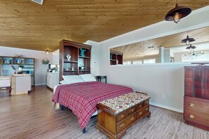 A bedroom with a wooden ceiling, a bed with a red checkered bedspread, a wooden chest of drawers, and a window with a view of the room. - Relaxing Waterfront Studio Cottage with Private Beach Access (Clinton)
