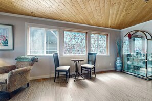 A room with a wooden ceiling, two windows with floral patterns, a small table, two chairs, a decorative glass cabinet, and a framed picture on the wall. - Relaxing Waterfront Studio Cottage with Private Beach Access (Clinton)