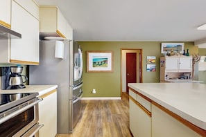 Een moderne keuken met roestvrijstalen apparatuur, een houten vloer en uitzicht op het platteland door een raam.