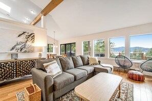 Ein modernes Wohnzimmer mit einem Ecksofa, einem Holztisch und Blick ins Freie durch große Fenster.