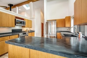 Eine moderne Küche mit Holzschränken, einem Edelstahlkühlschrank und einer schwarzen Arbeitsplatte.