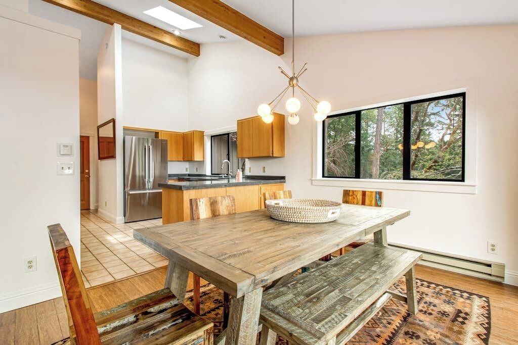 Una cocina moderna con armarios de madera, un refrigerador de acero inoxidable y una zona de comedor con una mesa y bancos de madera.